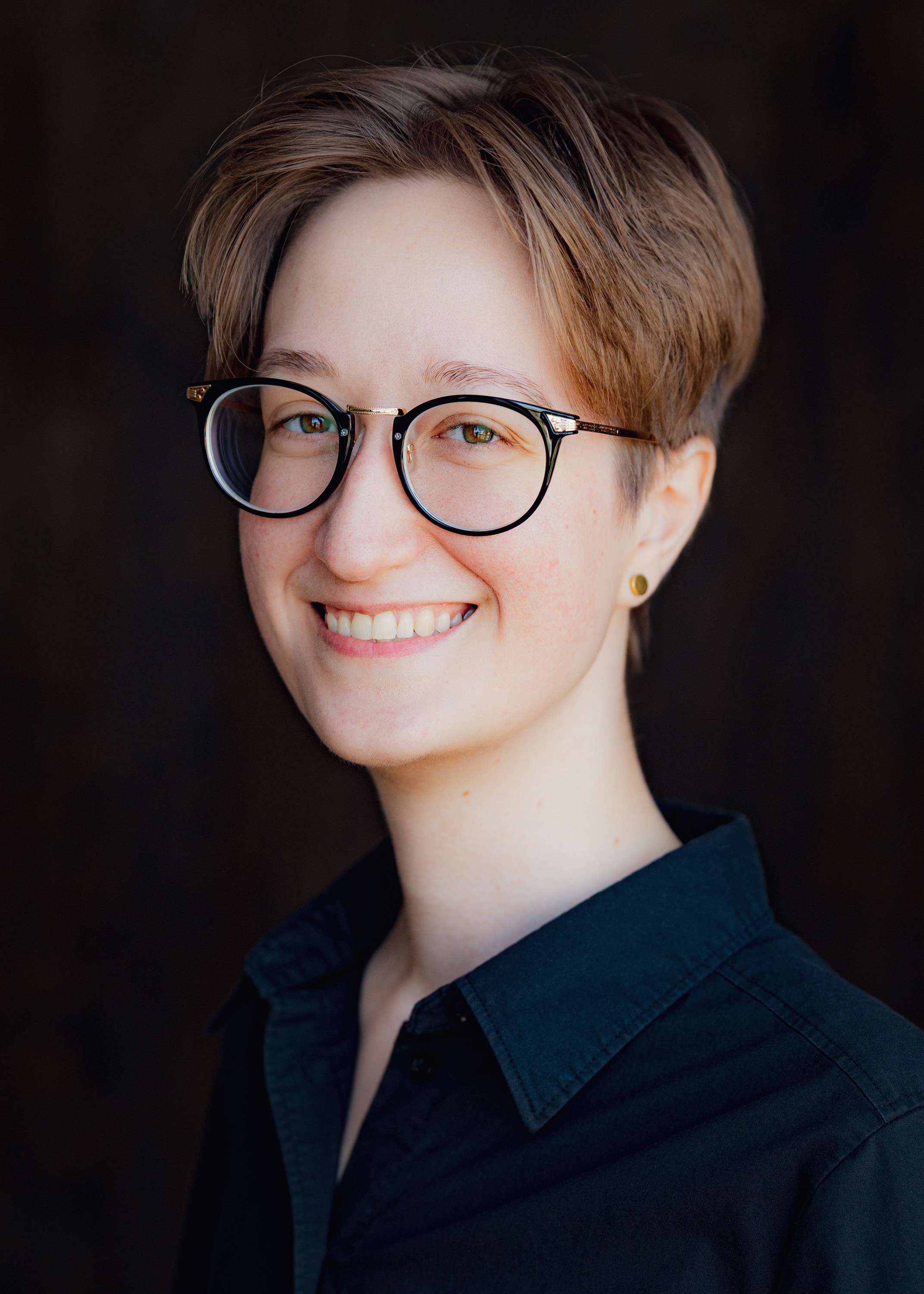 A person with short blonde hair and glasses smiling at the camera